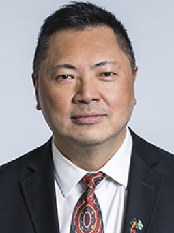 A close up of the front of a man from his chest up, with short back hair.