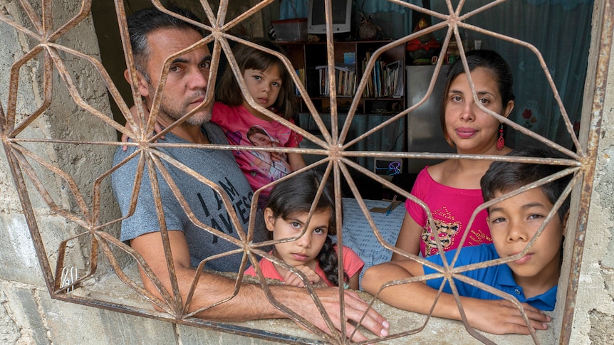 A man a woman, two little girls and a boy look through a barred window