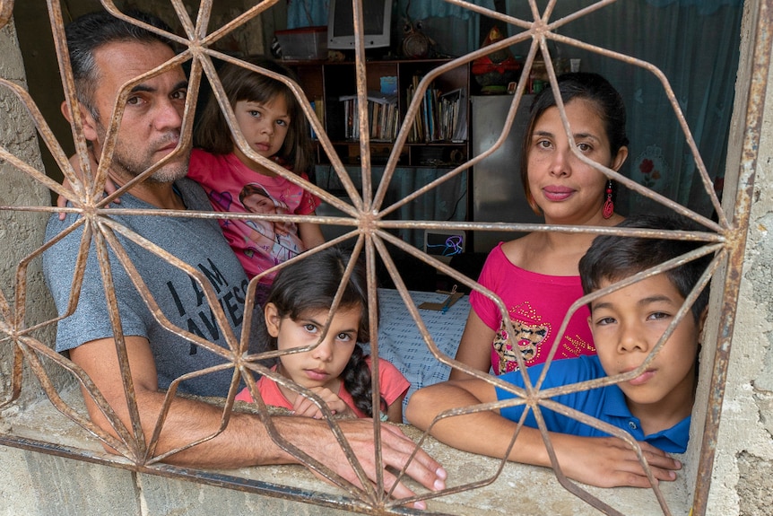 A man a woman, two little girls and a boy look through a barred window