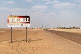 A sign that says "Welcome to Birdsville" standing on the side of an outback highway.