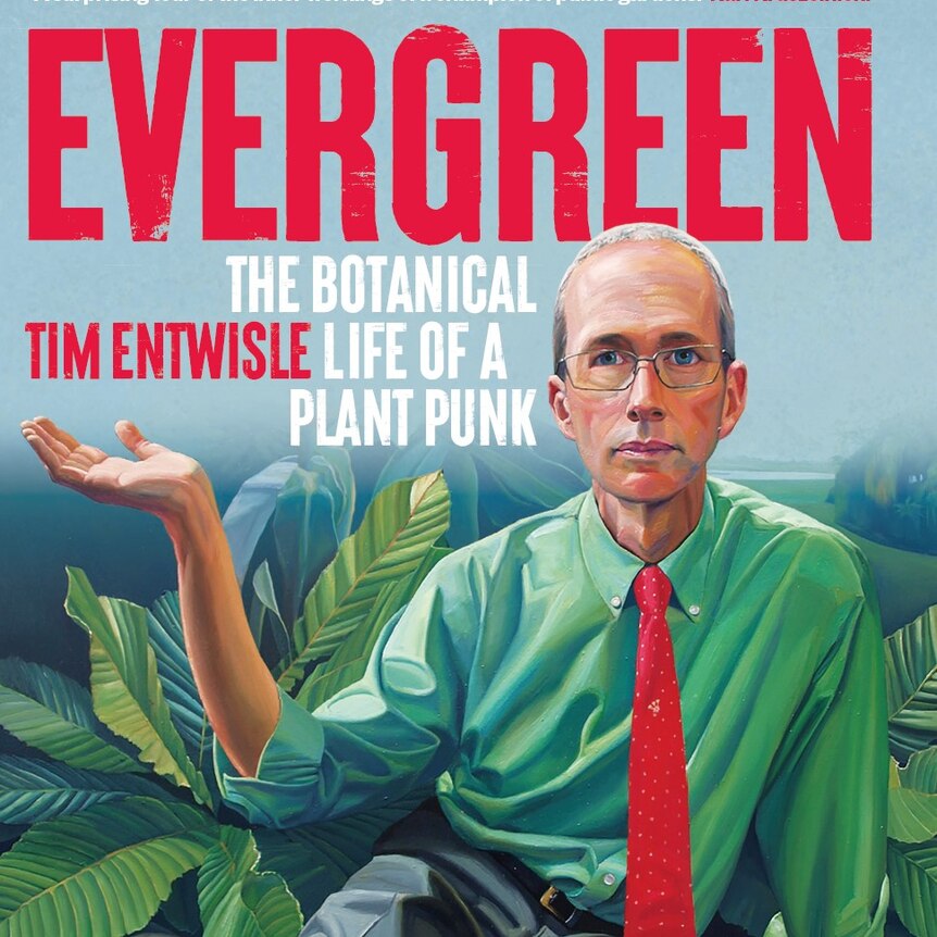 Tim Entwisle sitting on a plant and holding the title with one hand. 