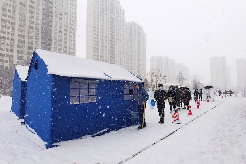 Residents line up at a makeshift nucleic acid testing site amid snowfall.