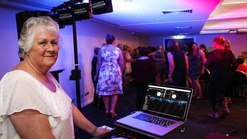 An older woman is controlling a DJ desk at an indoor party