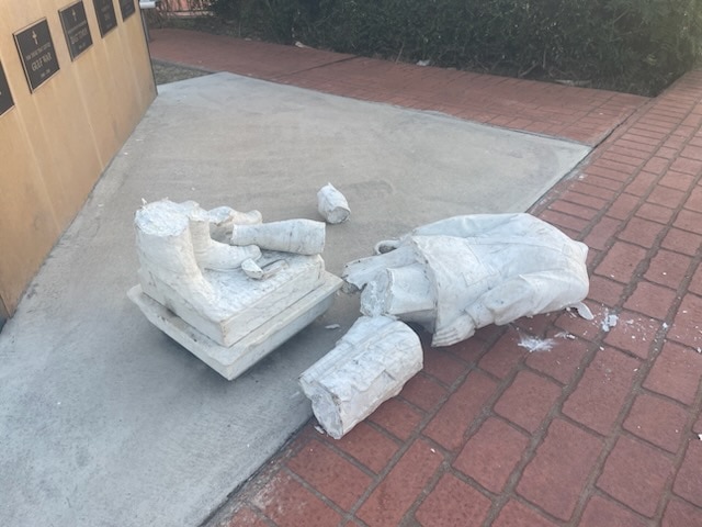 Uma estátua de pedra está em pedaços depois de ser esmagada contra um chão de tijolo e concreto.