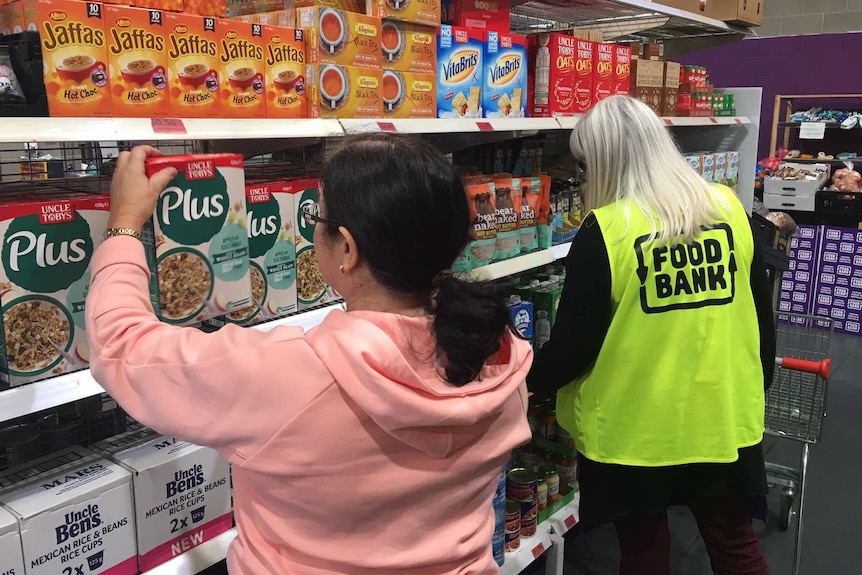 Two people grabbing products off a shelf at Foodbank SA