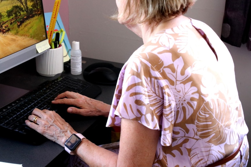 A woman wearing a brown and white floral top sits in front of a computer.