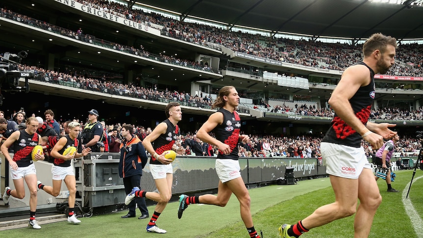 Essendon Bombers players run onto the MCG turf in front of a big crowd for their Anzac Day AFL game against Collingwood.