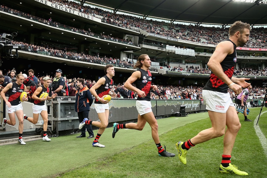 Les joueurs d'Essendon Bombers courent sur le gazon du MCG devant une grande foule pour leur match Anzac Day AFL contre Collingwood.