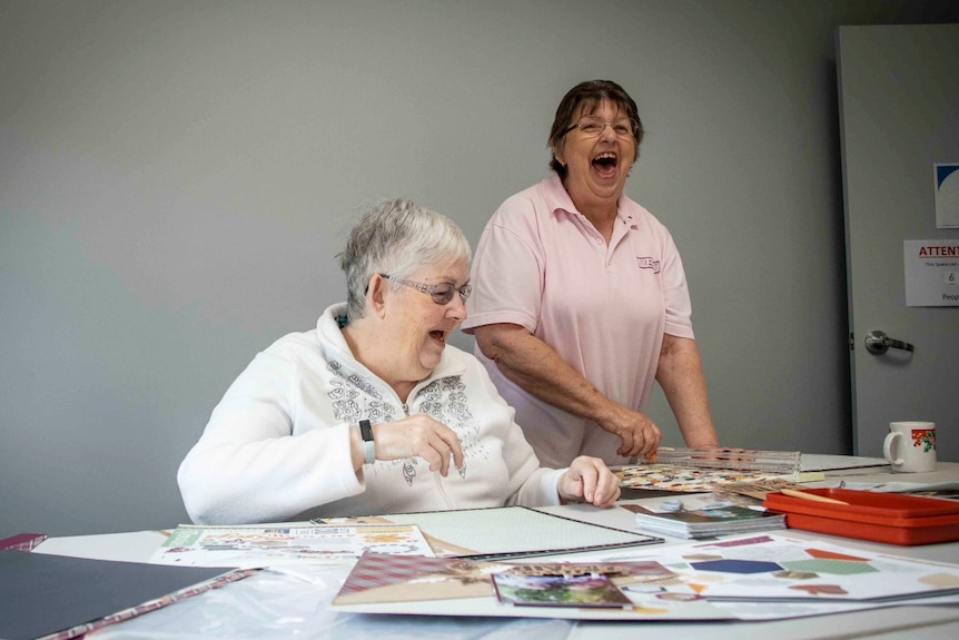 Two middle-aged women laugh while working on a scrapbook