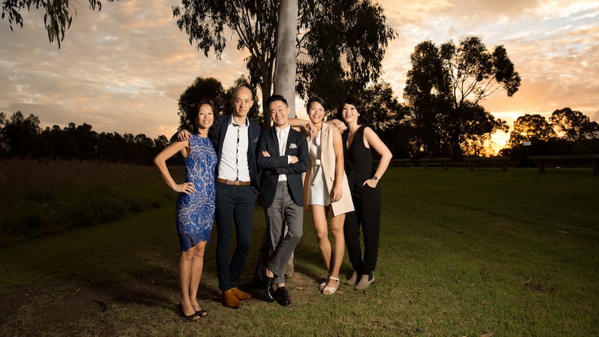 Five siblings standing together, laughing happily. 