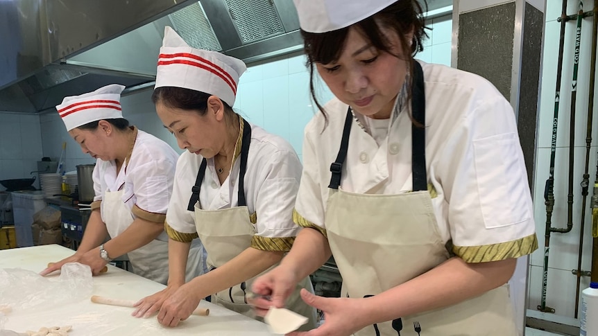 Three chefs prepare chinese dumplings with meat fillings in a commercial kitchen