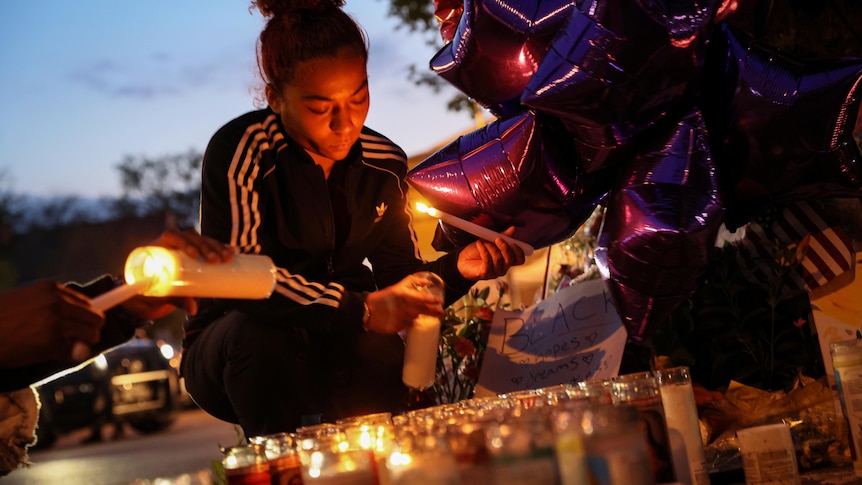 A woman lights a candle as dozens of other candles flicker.