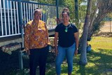 Two Indigenous women stand out the front of a house behind a garden gnome that says welcome