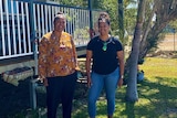 Two Indigenous women stand out the front of a house behind a garden gnome that says welcome