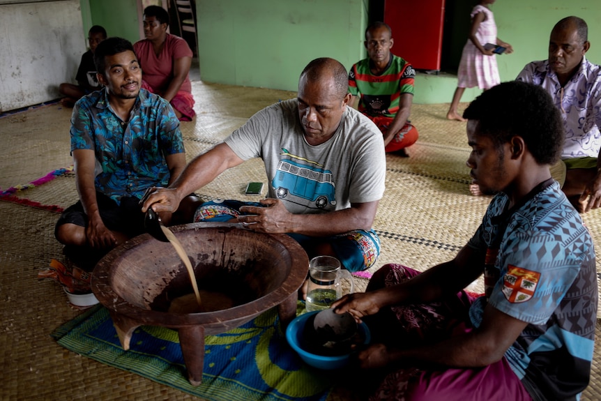 A traditional kava ceremony, men sit around a tanoa on a woven mat floor. 