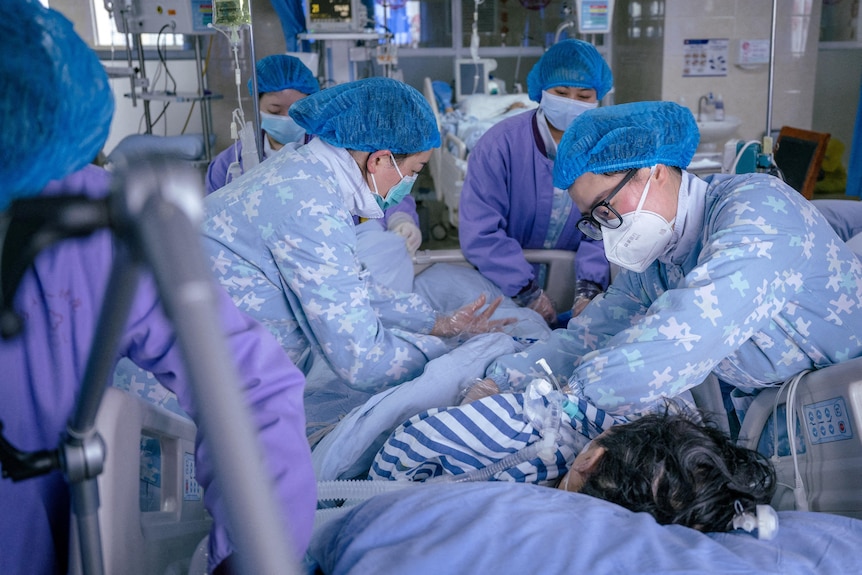Doctors wearing masks and personal protective equipment surround a patient lying down. 