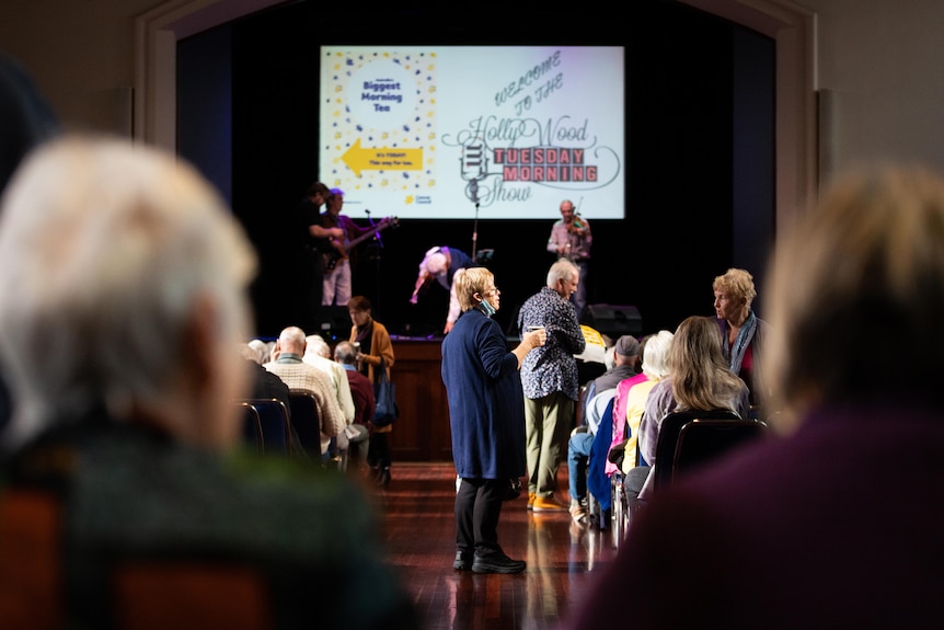 Crowds of older people, some wearing mask, in a performance hall.