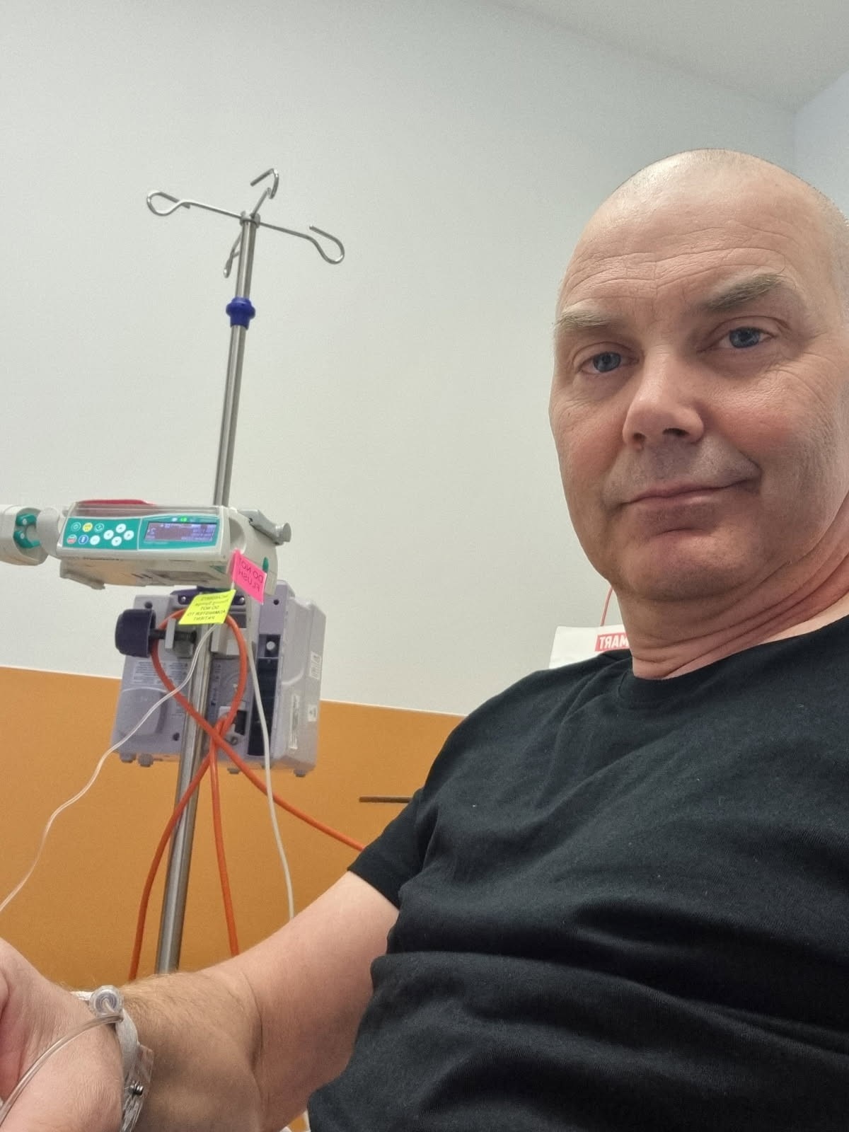 A bald man sitting in a hospital bed.