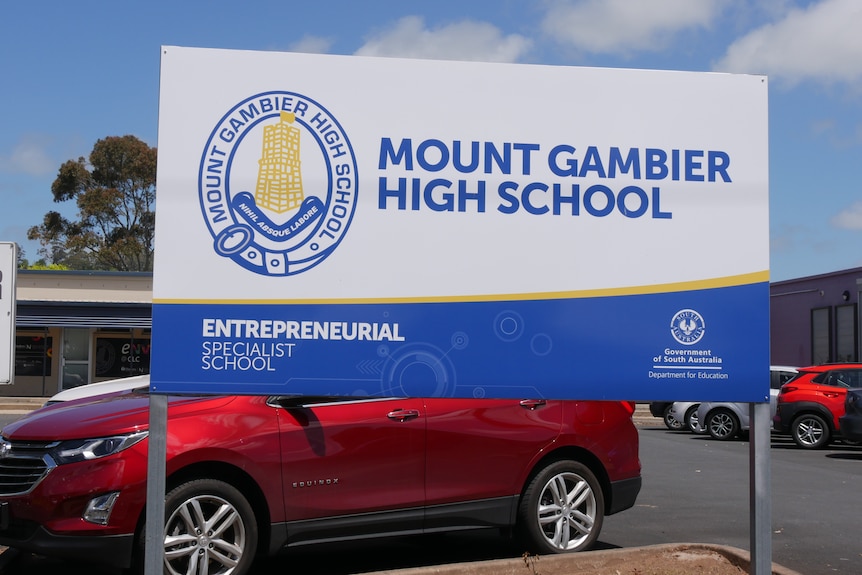 A white and blue sign reading "Mount Gambier High School" with a car park and buildings behind