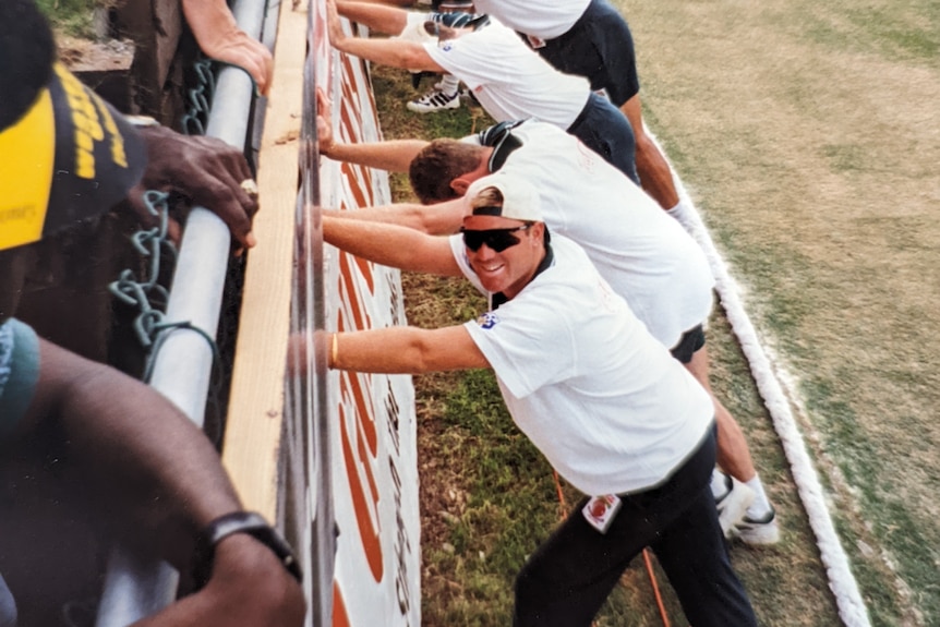 Shane Warne leans up against wall, facing camera smiling