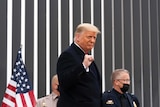 Donald Trump is standing in front of a wall as he pumps his fist and smiles