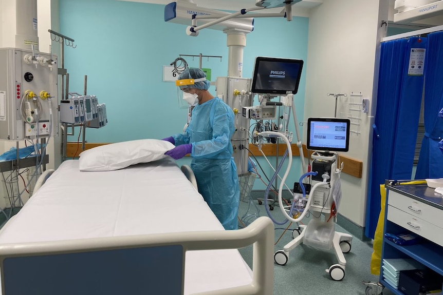 A nurse in full PPE holding a pillow on top of an empty ICU bed.