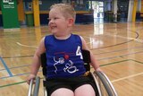five year old boy smiling in a wheelchair on a basketball court