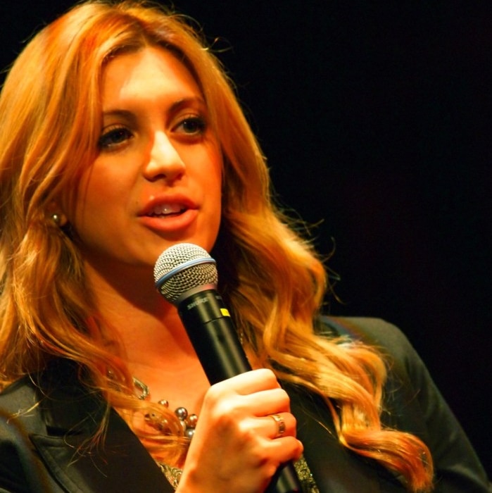 A women with blonde hair speaks into a microphone.