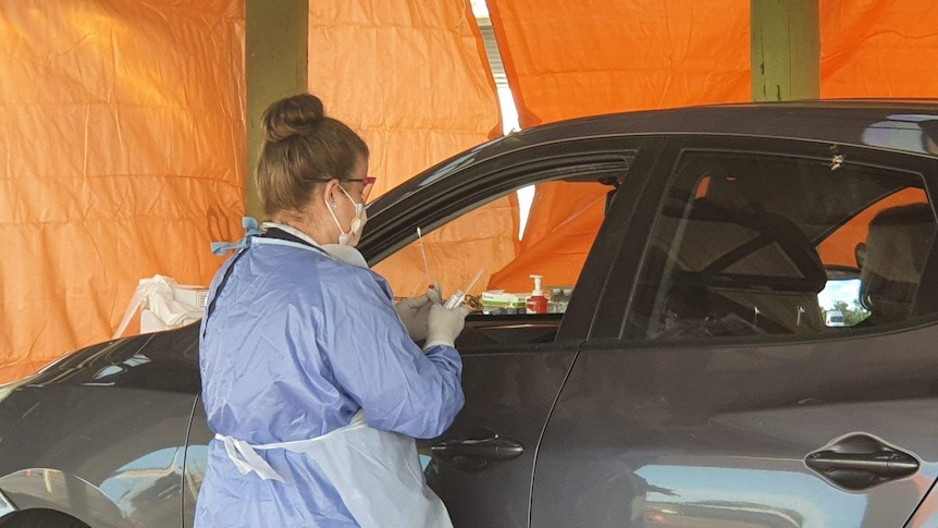 A health worker in protective clothing and a facemask swabs someone in a car at a fever clinic