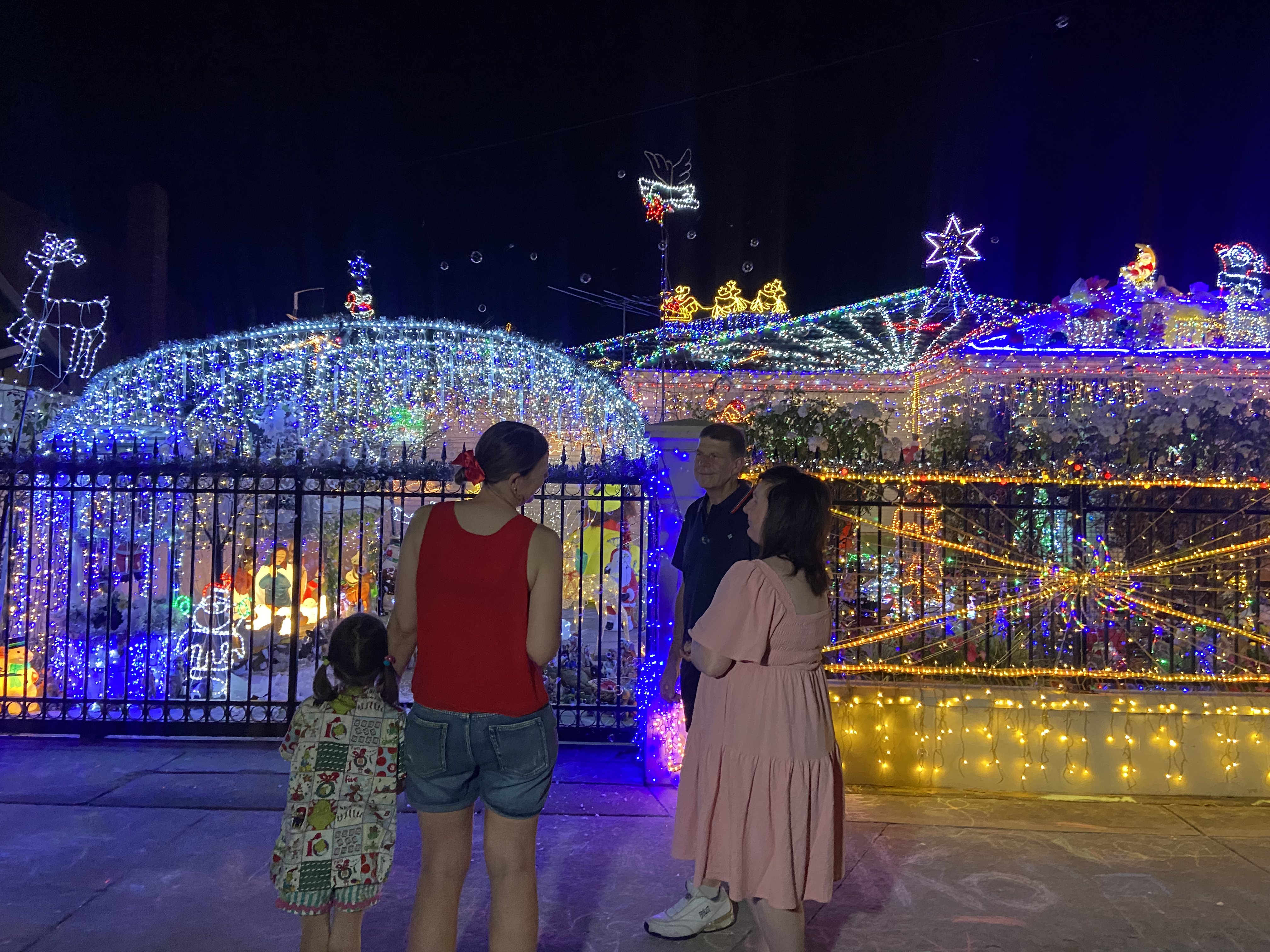 Uma família conversando com outra família do lado de fora de uma casa decorada com 50 mil luzes de Natal.