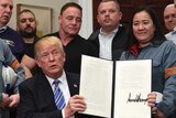 Surrounded by steel and aluminium workers, Donald Trump holds up a signed proclamation.