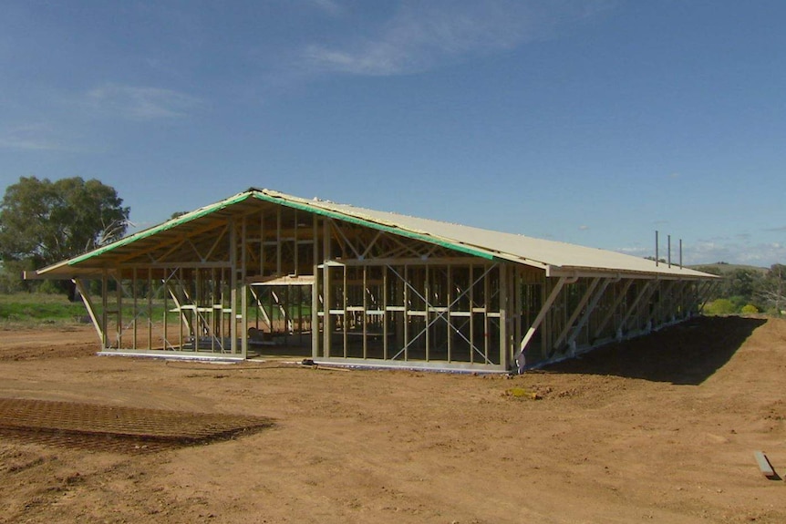 The framework of a house is in its building stages as it is surrounded by dirt in the country.