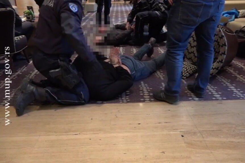 Police lean over Australian men laying facedown on the ground with their arms handcuffed behind their backs.