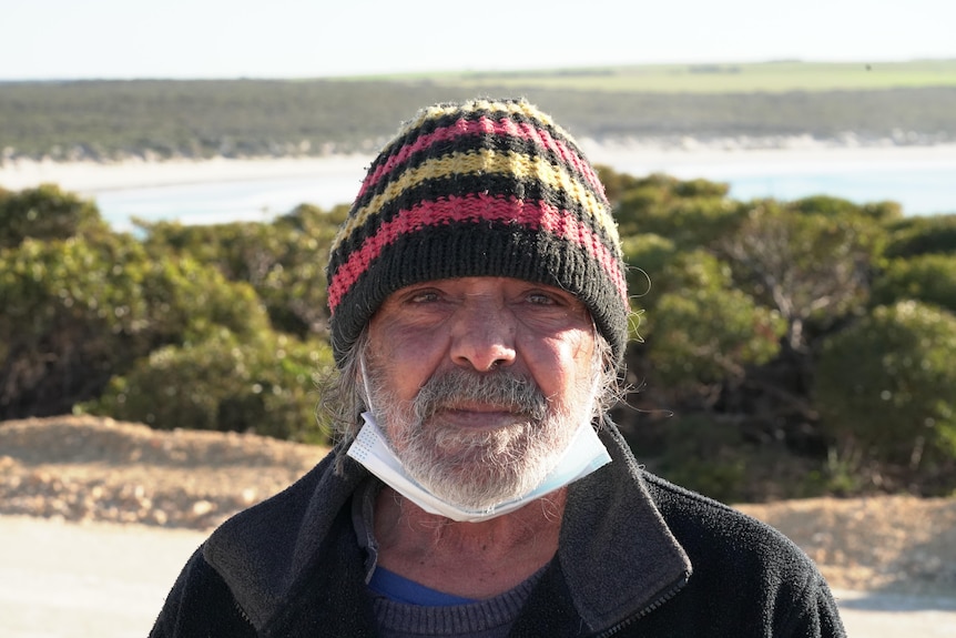 A man wearing a striped beanie and a mask pulled under his chin stares into the camera