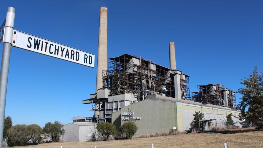 The Liddell Power Station is seen from across a road. The sky is blue and the grass is dry.