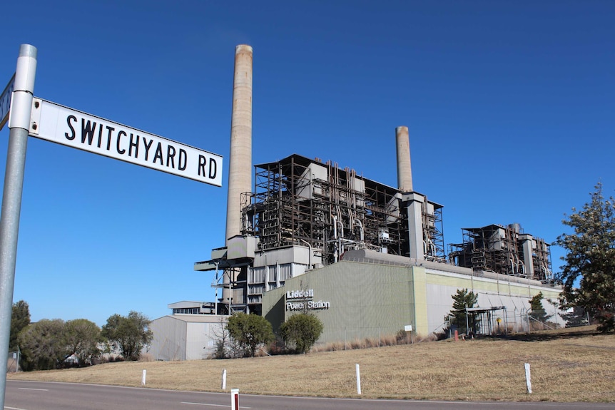 The Liddell Power Station is seen from across a road. The sky is blue and the grass is dry.