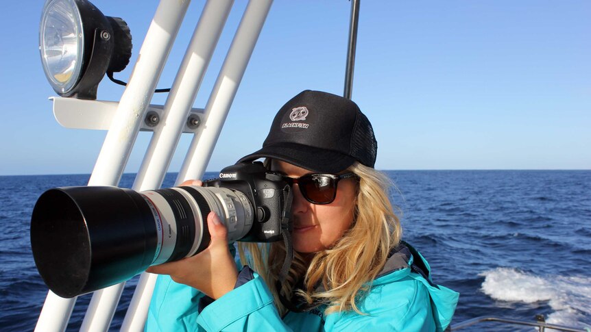 A woman standing on a boat taking a photo with a camera