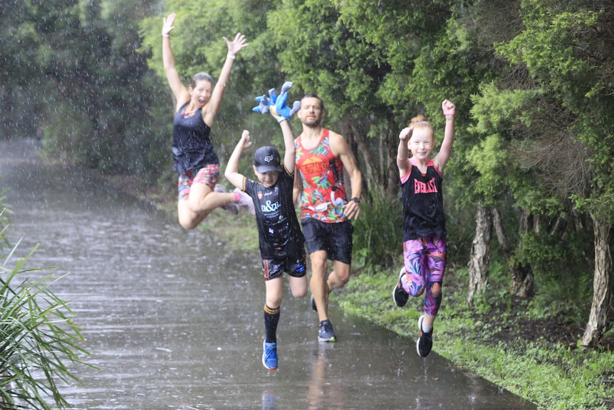 Two children pump the air while a man runs just behind them and a woman jumps in the air in the rain.