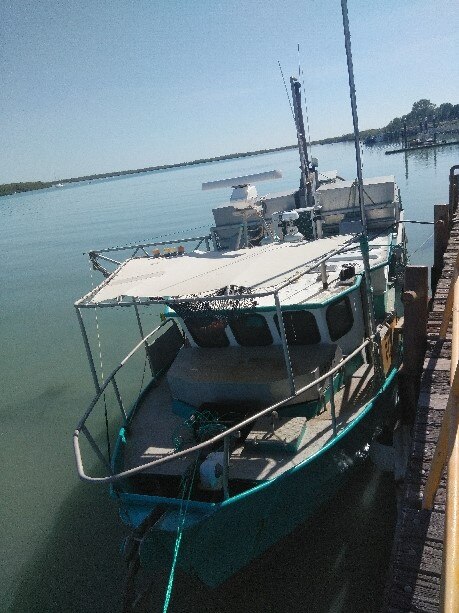 A 10-metre commercial fishing boat is tied by ropes alongside a wharf in port