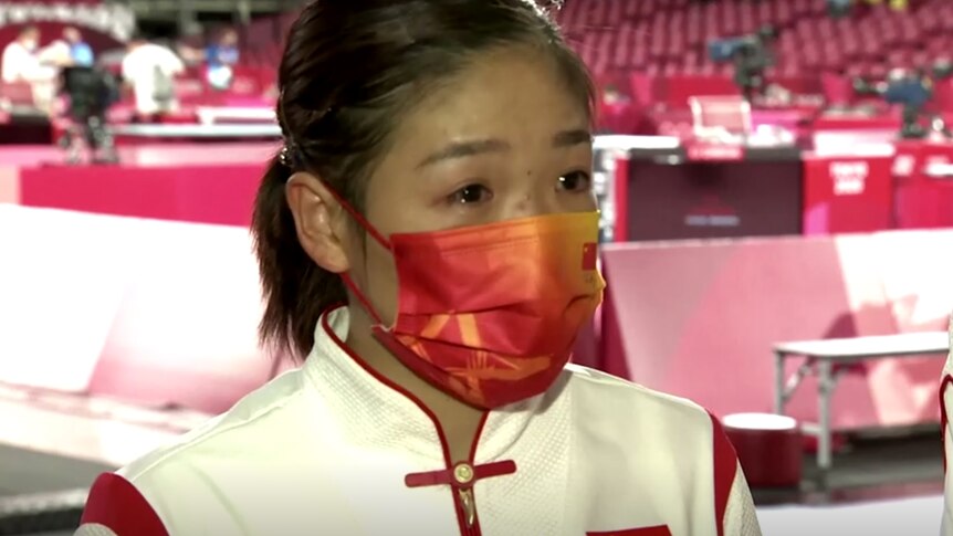 Liu Shiwen wearing a mask and with visible tears in her eyes at an Olympic venue.