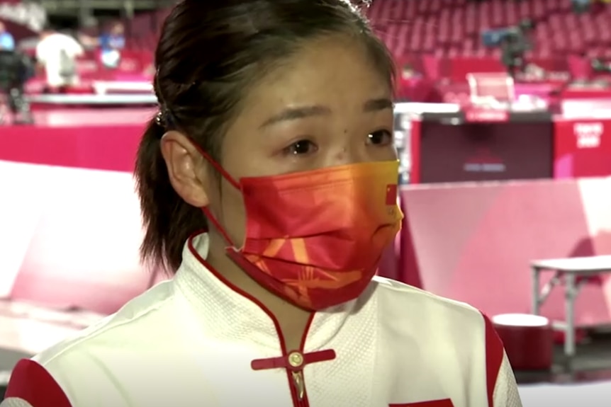 Liu Shiwen wearing a mask and with visible tears in her eyes at an Olympic venue.