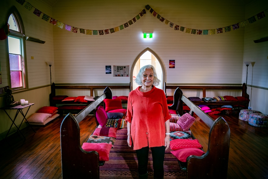 An older woman wearing a red shirt stands in a church hall