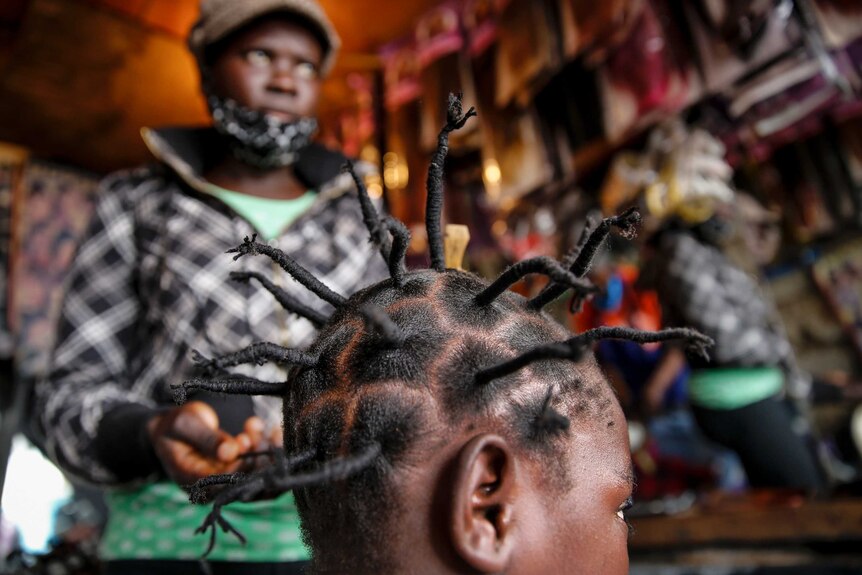 A girl gets her hair twisted into long things spikes at a hairdresser's salon.