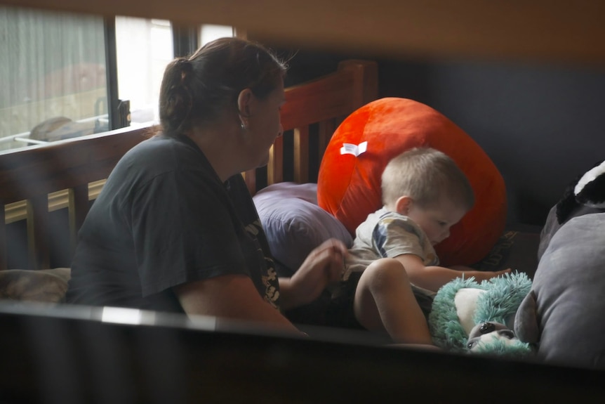 A woman sitting on a bed with her son and a teddy bear