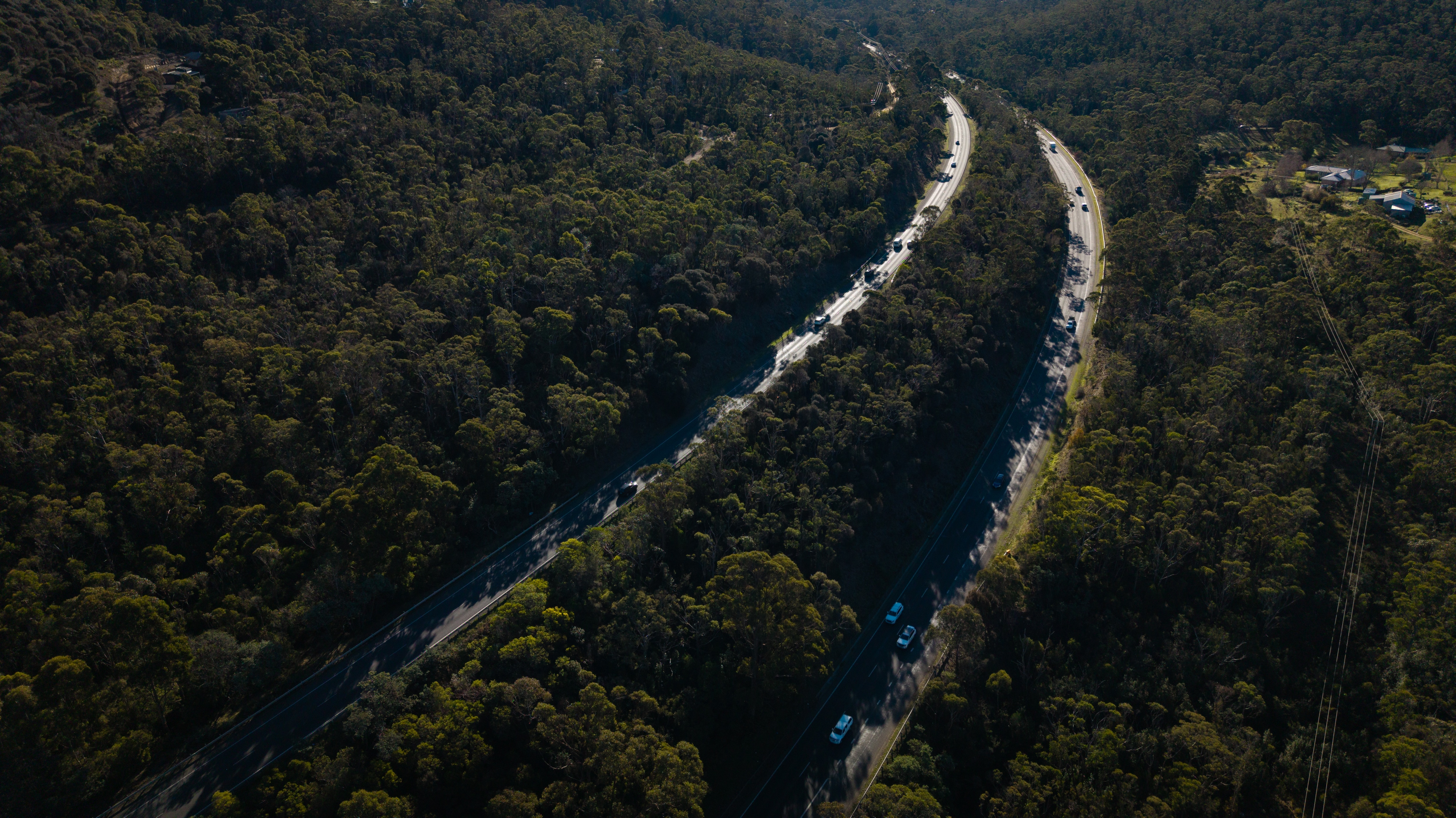 Aerial shot of a long road with busy traffic, winding through a hilly suburban neighbourhood