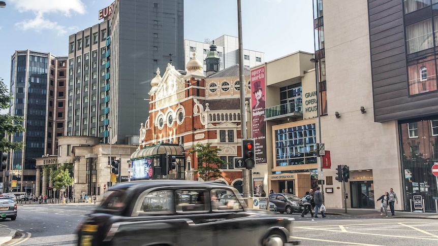 A black London cab whizzes past as you view a mix of medium-density modern buildings with a Victorian concert hall in the middle