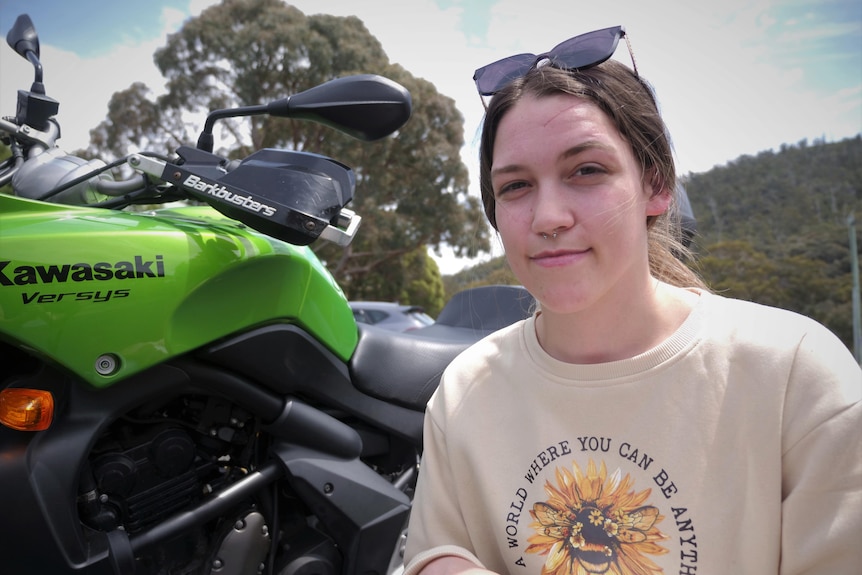A young woman crouched in front of a green motorbike, smiling to camera.