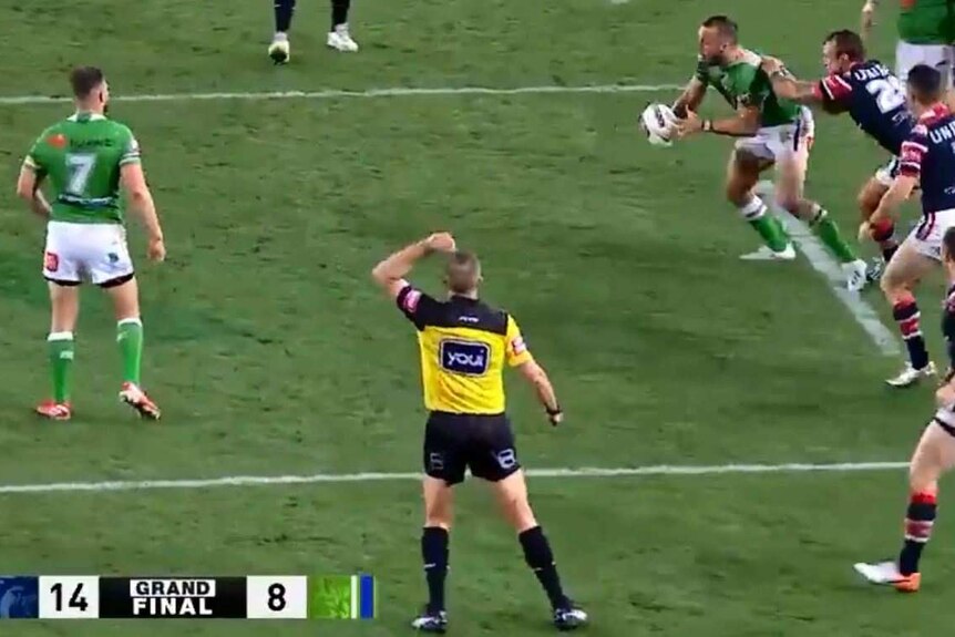 Referee Ben Cummins (bottom, in yellow and black) waves his hand in the air, signalling six more tackles for the Raiders.