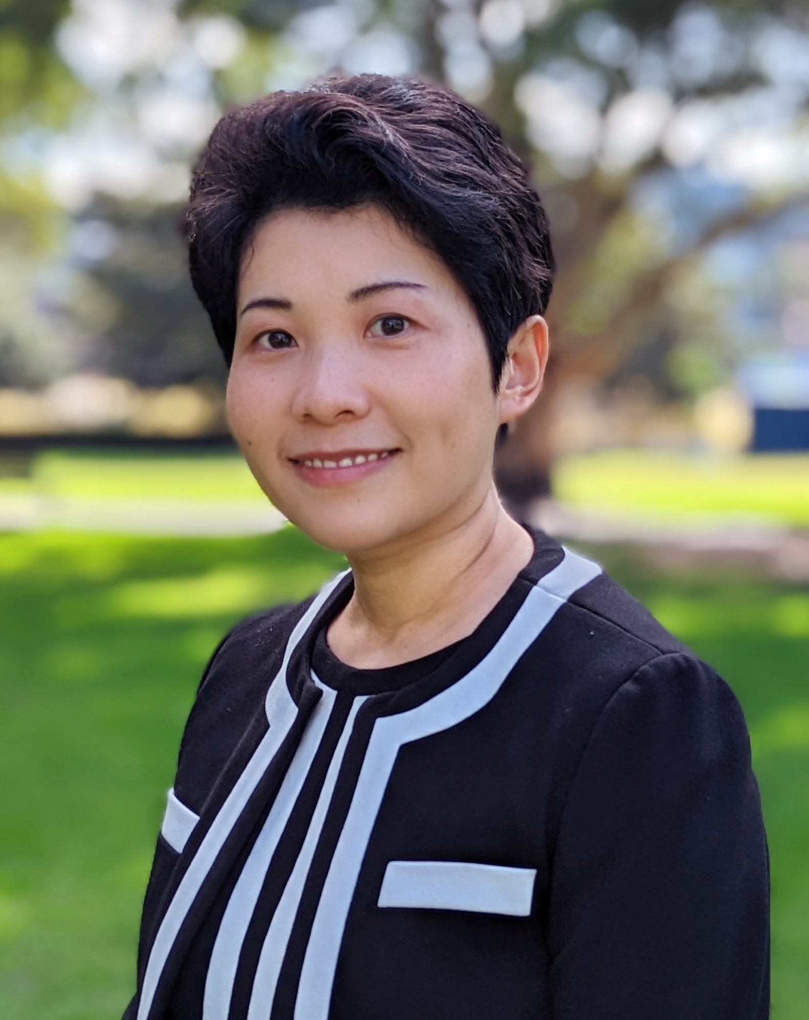 A woman with short black hair of Asian decent dressed in black and white in an outside area.