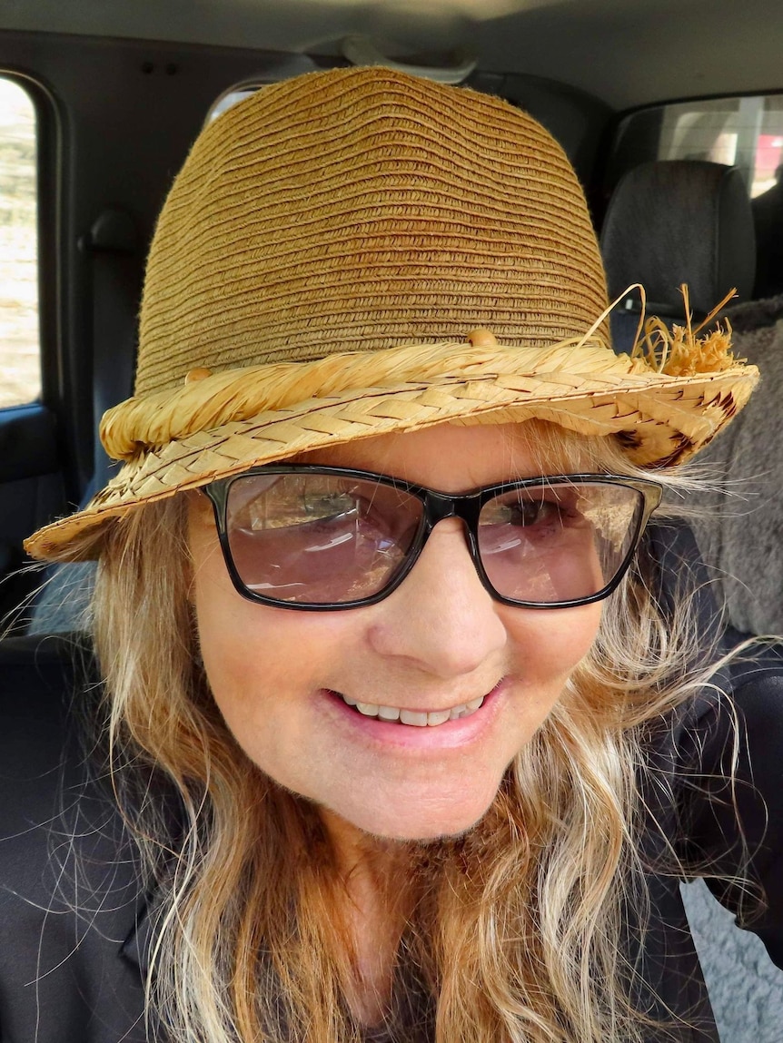 A woman with blonde hair smiling wearing a hat and sunglasses.